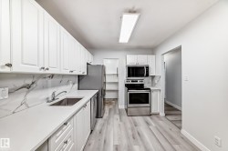 Kitchen featuring white shaker cabinetry, stainless steel appliances, light wood-finish flooring, and a marble-patterned backsplash - 