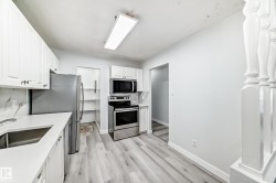 Kitchen featuring white cabinetry, stainless steel appliances, light-toned wood-finish flooring, and a stone-look backsplash - 