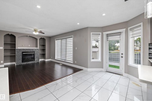 Open-concept living area featuring a dark wood-finish flooring, a fireplace with a dark tiled surround, and integrated arched shelving - 4831 154 Avenue, Edmonton, AB 