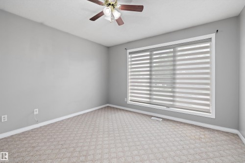 Spacious room featuring patterned carpet flooring, a ceiling fan with light fixture, and a large window with layered blinds - 4831 154 Avenue, Edmonton, AB 
