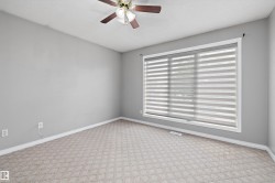 Spacious room featuring patterned carpet flooring, a ceiling fan with light fixture, and a large window with layered blinds - 