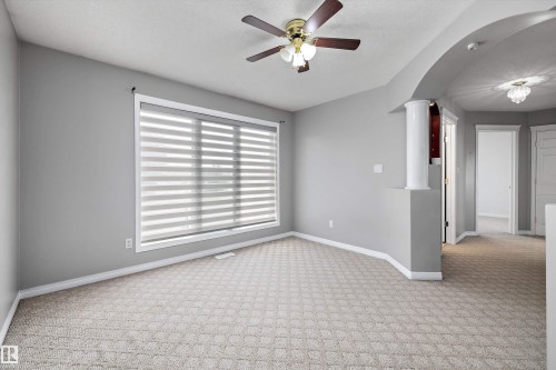 Carpeted room featuring a large window with horizontal blinds, a ceiling fan with light fixture, and an arched doorway - 4831 154 Avenue, Edmonton, AB 