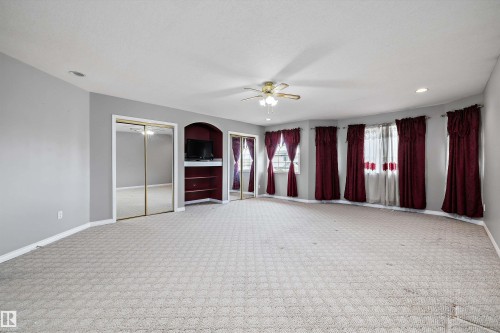 Spacious room featuring light gray walls, patterned carpeting, and multiple windows - 4831 154 Avenue, Edmonton, AB 