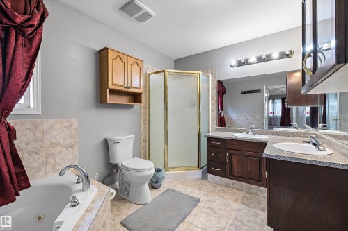 Full bathroom featuring a corner shower with a gold-finish frame, a built-in tub with a tiled surround, a double vanity with integrated sinks and dark wood cabinetry, and a mirrored wall - 4831 154 Avenue, Edmonton, AB 