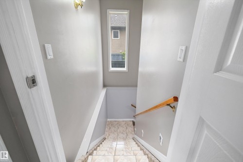 Stairwell featuring tile flooring, light neutral wall paint, and a wood handrail - 4831 154 Avenue, Edmonton, AB 