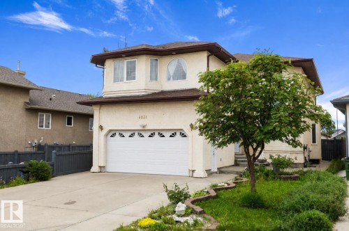 Two-story residence featuring a stucco exterior, integrated garage with decorative window inserts, concrete driveway, and mature landscaping - 4831 154 Avenue, Edmonton, AB 