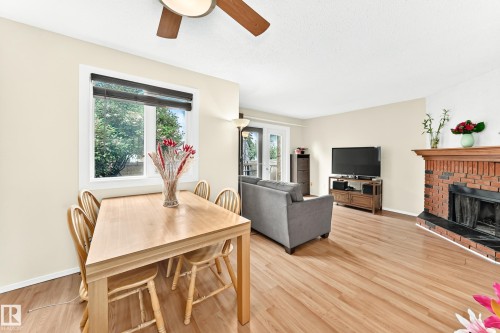 Spacious open-concept living area featuring wood-finish flooring, a brick fireplace with a black hearth, and a contemporary ceiling fan - 102 Royal Terrace, Edmonton, AB 
