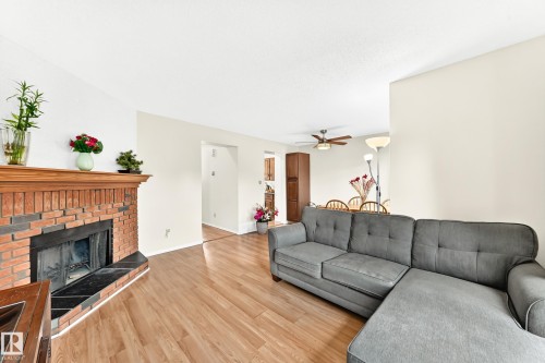 Living area featuring wood-finish flooring, a brick fireplace with a wood mantle, and an open doorway leading to a dining space with a ceiling fan - 102 Royal Terrace, Edmonton, AB 