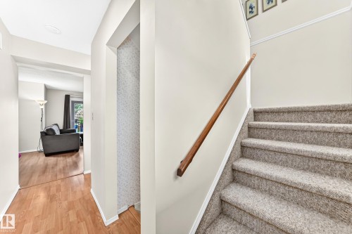 Carpeted staircase with wooden handrail, featuring light neutral wall paint and white trim - 102 Royal Terrace, Edmonton, AB 
