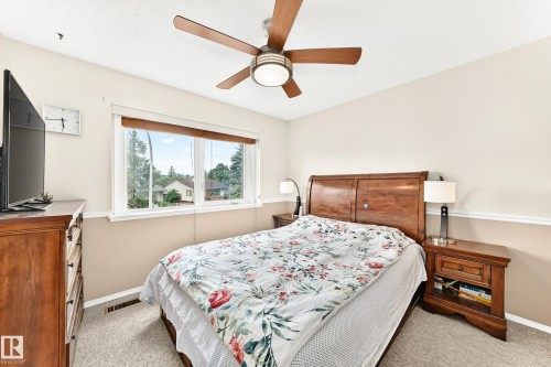 Bedroom featuring a wood-finish bed frame, neutral-toned walls with chair rail molding, carpet flooring, a ceiling fan with integrated lighting, and a large window with white trim - 102 Royal Terrace, Edmonton, AB 