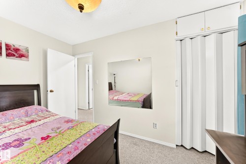 Bedroom featuring wall-to-wall carpeting, light neutral wall paint, and a built-in accordion-door closet with overhead cabinetry - 102 Royal Terrace, Edmonton, AB 