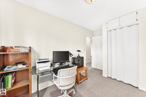 Carpeted room with a built-in closet featuring white bifold doors and overhead cabinetry - 102 Royal Terrace, Edmonton, AB 
