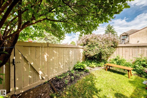 Private backyard featuring a wood fence, mature tree with green foliage, and garden beds with plantings - 102 Royal Terrace, Edmonton, AB 