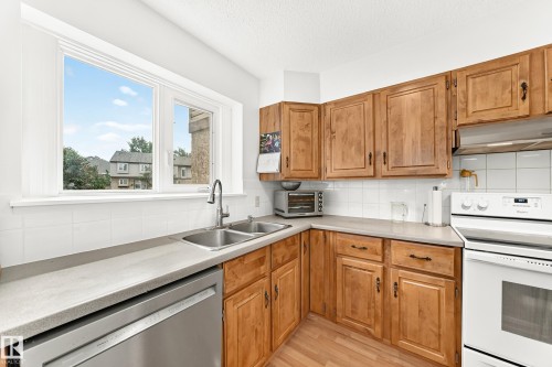 Kitchen featuring ample wood cabinetry, a dual basin stainless steel sink with a gooseneck faucet, light countertops, a white subway tile backsplash, and wood-finish flooring - 102 Royal Terrace, Edmonton, AB 