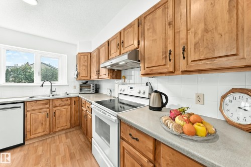 Kitchen featuring wood-finish cabinetry, light-toned countertops, and a white tile backsplash - 102 Royal Terrace, Edmonton, AB 