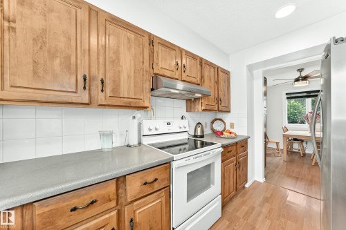 Kitchen featuring natural wood cabinetry, white tile backsplash, light-toned countertops, and wood-finish flooring - 102 Royal Terrace, Edmonton, AB 