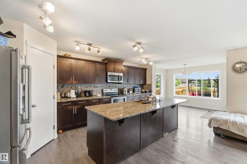 Kitchen featuring a large central island with a stone countertop, dark wood-finish cabinetry, stainless steel appliances, and wood-finish flooring - 5120 19 Avenue, Edmonton, AB 
