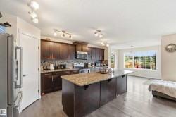 Kitchen featuring a large central island with a stone countertop, dark wood-finish cabinetry, stainless steel appliances, and wood-finish flooring - 