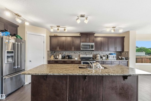 Kitchen island with an undermount sink, granite-style countertop, and dark wood-finish cabinetry - 5120 19 Avenue, Edmonton, AB 