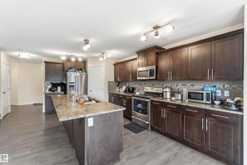 Kitchen featuring dark wood cabinetry with crown molding, stainless steel appliances, a multi-tone tile backsplash, and a central island with a light-colored stone countertop - 5120 19 Avenue, Edmonton, AB 