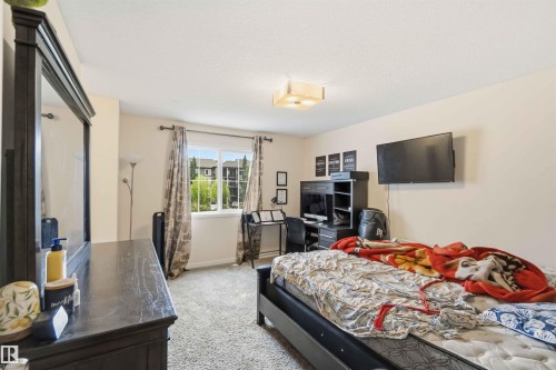 Carpeted room with a ceiling-mounted light fixture, a window with exterior views, and a wall-mounted television - 5120 19 Avenue, Edmonton, AB 