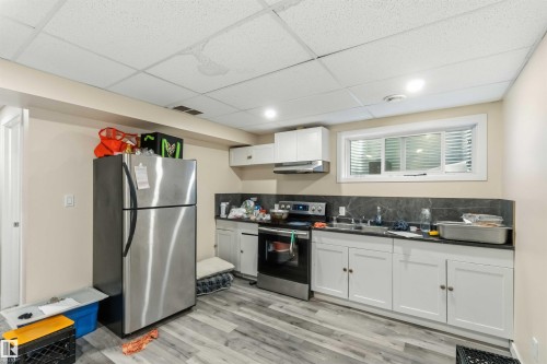 Kitchenette featuring white cabinetry, a stainless steel refrigerator, and a built-in range - 5120 19 Avenue, Edmonton, AB 
