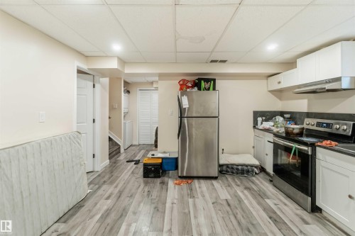 Kitchenette area featuring stainless steel appliances, white cabinetry, dark countertops, and wood-finish flooring - 5120 19 Avenue, Edmonton, AB 