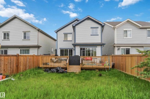 Rear exterior featuring light grey siding with dark trim accents, a full-width wooden deck, and a fenced backyard - 5120 19 Avenue, Edmonton, AB 