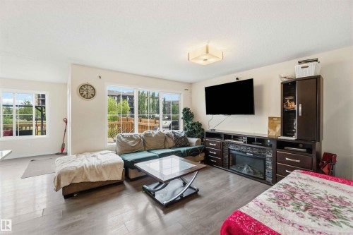 Spacious living area featuring light wood-finish flooring, large windows, recessed lighting, and an entertainment console with an integrated fireplace - 5120 19 Avenue, Edmonton, AB 