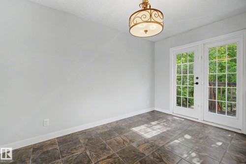 Room featuring French doors with grid-patterned glass, a ceiling-mounted semi-flush light fixture with an ornate metal frame, and large format floor tiles - 1511 75 Street, Edmonton, AB 