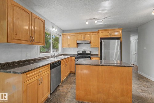 Kitchen featuring wood cabinetry, dark stone countertops, tile flooring, stainless steel appliances, and a central island - 1511 75 Street, Edmonton, AB 