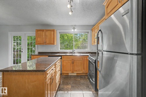 Kitchen featuring wood cabinetry, granite-finish countertops, stainless steel appliances, and tile flooring - 1511 75 Street, Edmonton, AB 