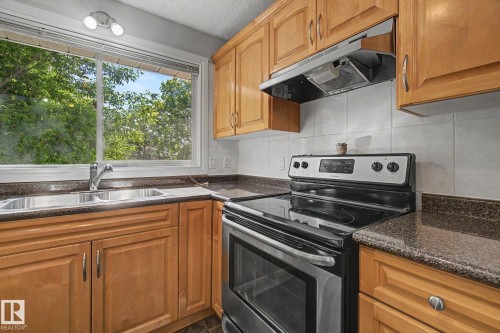 Kitchen featuring wood cabinetry, dark speckled countertops, and a white tile backsplash - 1511 75 Street, Edmonton, AB 