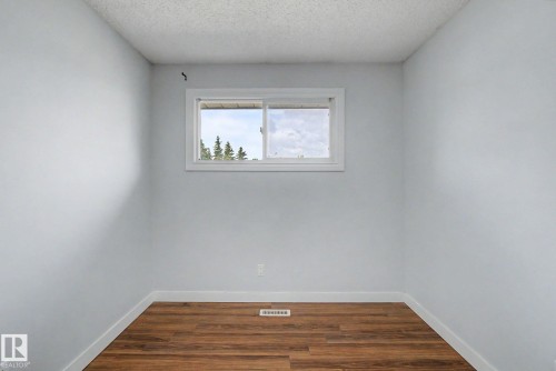 Bright interior room featuring a white-framed window, wood-finish flooring, white baseboards, and light-colored walls - 1511 75 Street, Edmonton, AB 