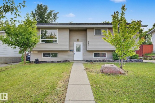 Split-level residence featuring light-toned horizontal siding, a central white entry door, and a concrete pathway - 1511 75 Street, Edmonton, AB 