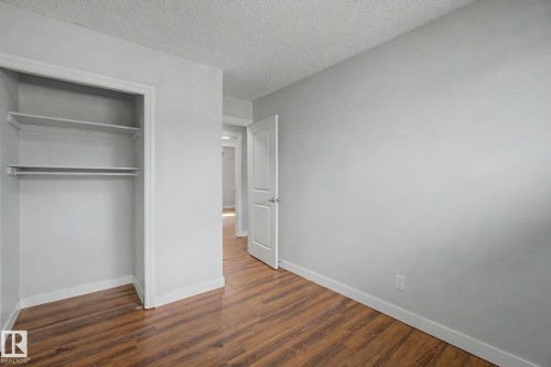 Bedroom featuring wood-finish flooring, a built-in closet with shelving and hanging rod, light gray wall paint, and white trim - 1511 75 Street, Edmonton, AB 