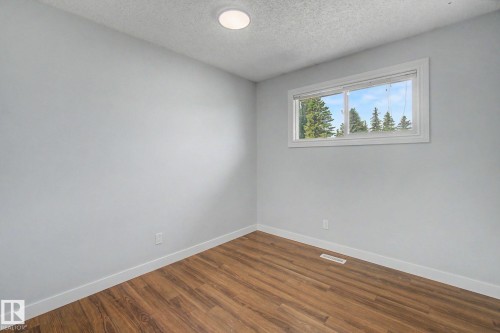 Room featuring a horizontal window, wood-finish flooring, light grey walls, white baseboards, and a recessed ceiling light - 1511 75 Street, Edmonton, AB 