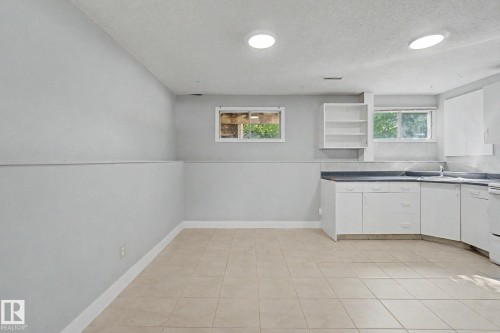 Kitchenette featuring white cabinetry, dark countertops, a stainless steel sink, and ceramic tile flooring - 1511 75 Street, Edmonton, AB 