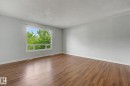 Spacious room featuring wood-finish flooring, light grey walls, and a large window with white trim - 1511 75 Street, Edmonton, AB 