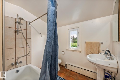Bathroom featuring a white pedestal sink with chrome faucet, a standard toilet, and a white bathtub with light beige tiled surround - 11022 110 Avenue, Edmonton, AB 