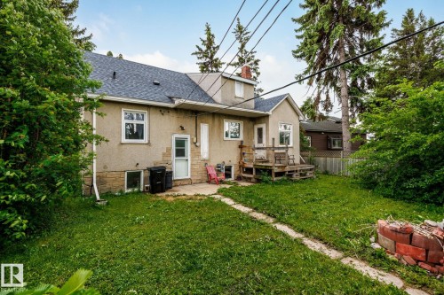 Rear exterior featuring stucco siding, stone foundation, a wooden deck, and a shingled roof - 11022 110 Avenue, Edmonton, AB 