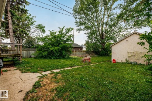 Fenced backyard featuring a concrete walkway, mature trees, and a detached outbuilding - 11022 110 Avenue, Edmonton, AB 