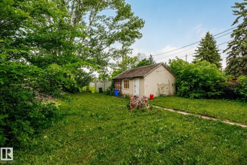 Detached storage building with a stucco exterior and shingled roof, set on a grassy parcel with mature trees - 11022 110 Avenue, Edmonton, AB 