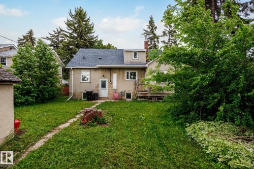 Expansive backyard with a manicured lawn, established trees, a concrete pathway, a rear patio, and a shingled roofline - 11022 110 Avenue, Edmonton, AB 