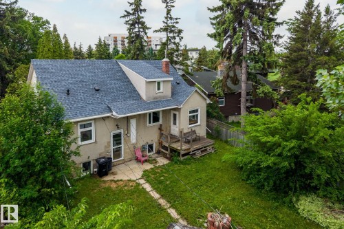 Rear exterior showcasing a shingle roof, stucco siding, and a partial stone facade - 11022 110 Avenue, Edmonton, AB 