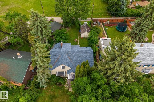 Property featuring a blue shingle roof, light-colored exterior, and surrounding mature trees - 11022 110 Avenue, Edmonton, AB 