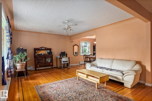 Spacious living area featuring wood-finish flooring, a ceiling fan, and large windows - 11022 110 Avenue, Edmonton, AB 