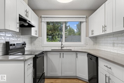 Modern kitchen featuring white shaker cabinetry, light-toned countertops, a white subway tile backsplash, and wood-finish flooring - 15112 80 Street, Edmonton, AB 