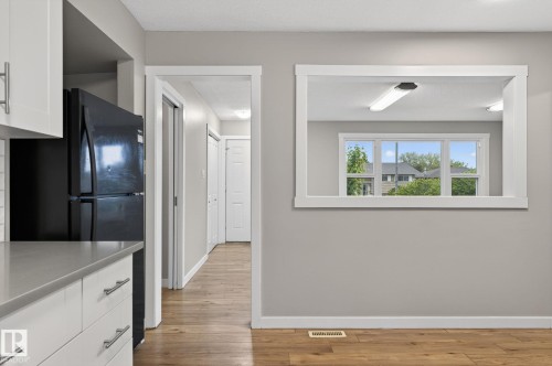 Contemporary kitchen featuring white cabinetry with silver hardware, light gray countertops, and a black refrigerator - 15112 80 Street, Edmonton, AB 