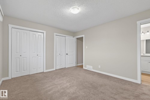 Carpeted room featuring neutral wall tones, two sets of white bi-fold closet doors, and white trim throughout - 15112 80 Street, Edmonton, AB 